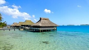 Bungalows sobre el agua con techos de paja y pasarelas de madera que se extienden en aguas turquesas cristalinas.