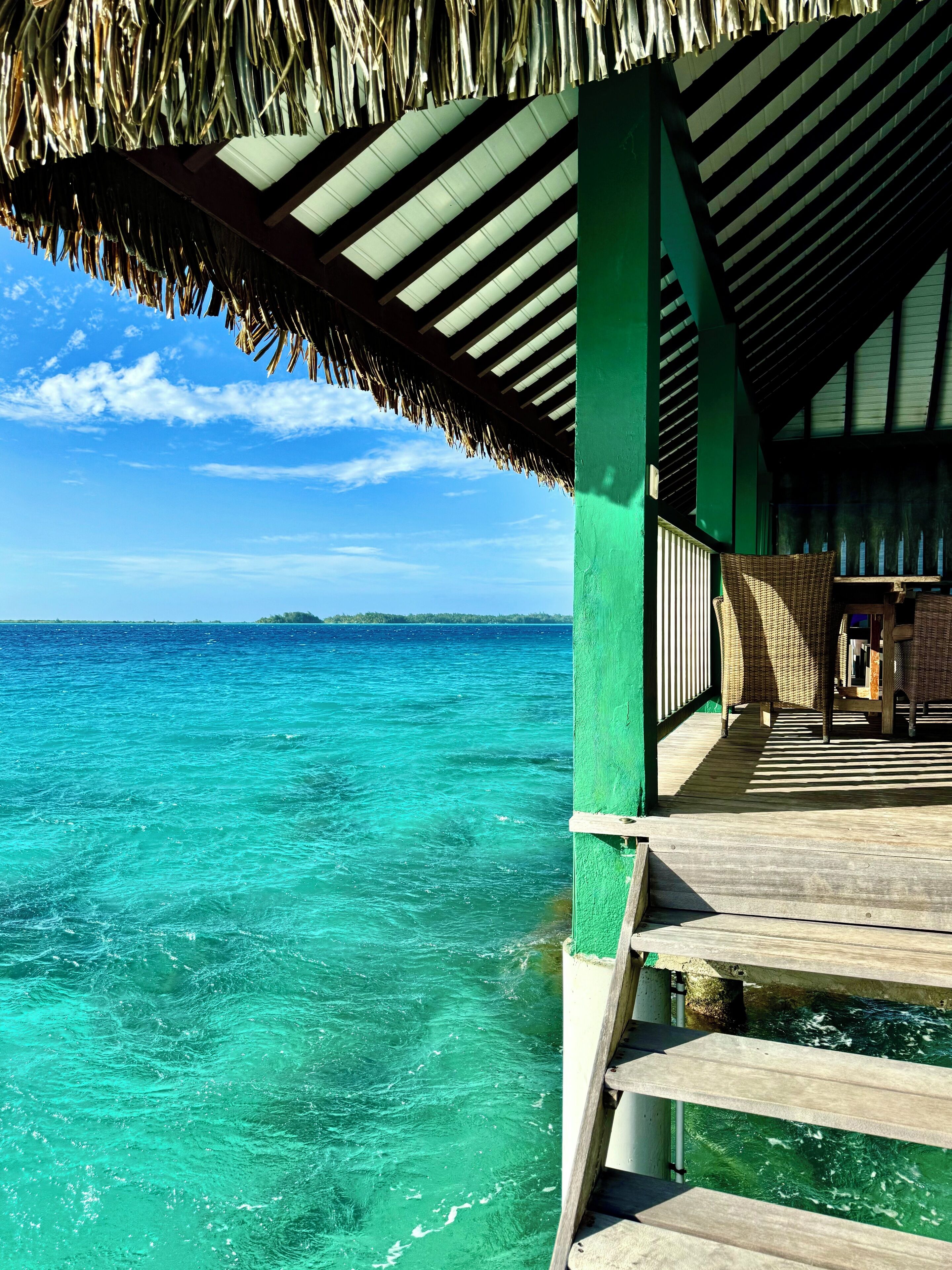 A wooden deck with a thatched roof overlooking turquoise waters.