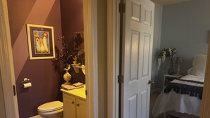 A bathroom with a toilet, sink, and mirror. There is a towel rack with towels and a vase with flowers. -  Savannah Suite  (Kennesaw)