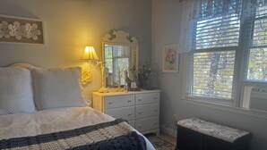 A bedroom with a bed, bedside lamp, dresser, bench, and a window with blinds. -  Savannah Suite  (Kennesaw)