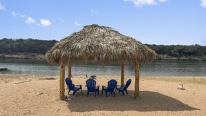 A beach with a thatched hut, blue chairs, and a table. - Waterfront, gorgeous sunsets, sandy beach, dogs allowed. (Kingsland)