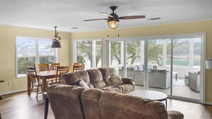 A spacious living room with a brown leather sofa, a dining table with chairs, and a ceiling fan. - Waterfront, gorgeous sunsets, sandy beach, dogs allowed. (Kingsland)