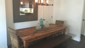 Ein Holzespeisetisch mit drei Glasflaschen, ein gewebter Stuhl und eine hängende Leuchte.