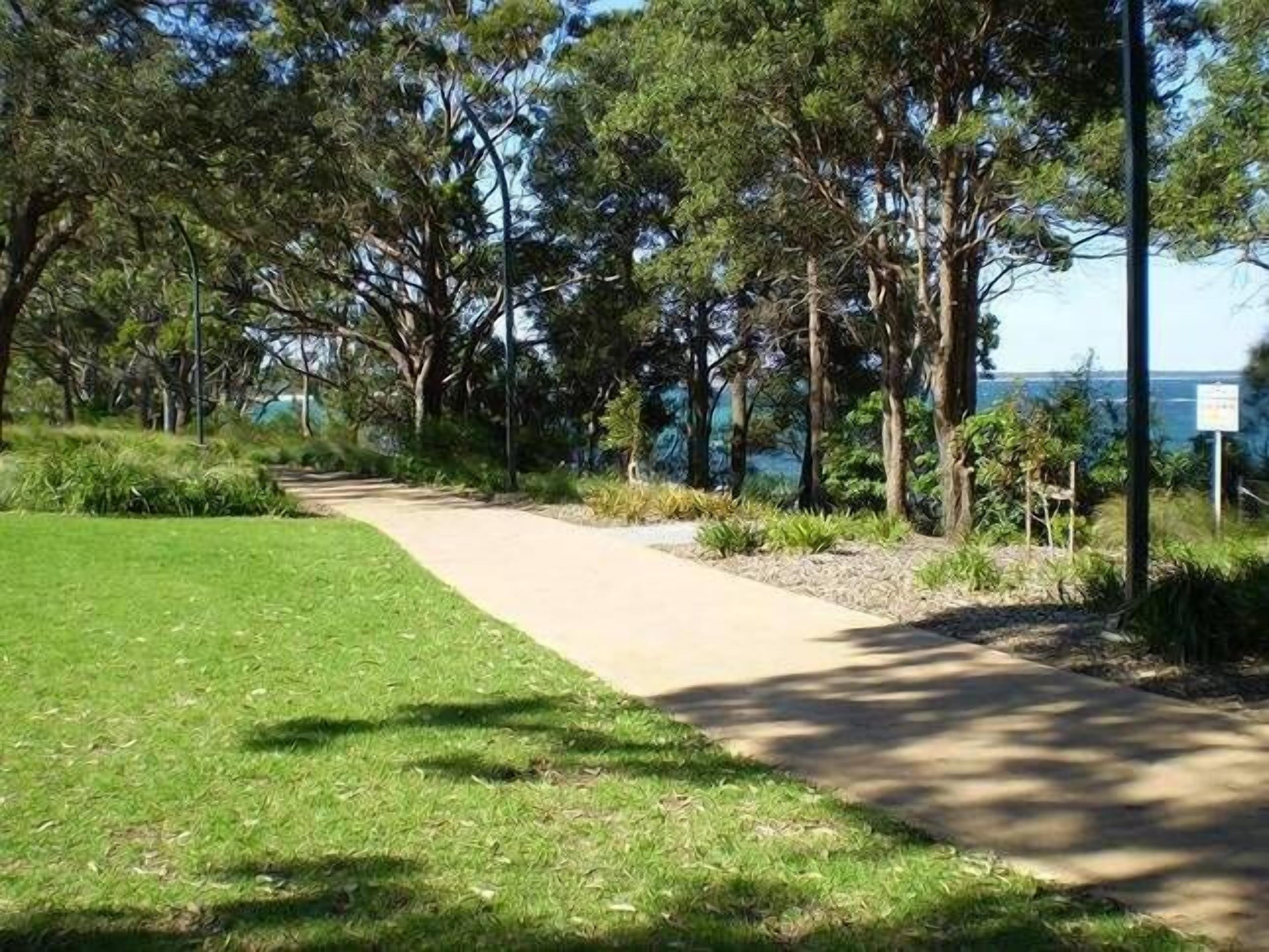 Ein Weg, der durch einen Park mit Bäumen und Blick auf das Meer führt.