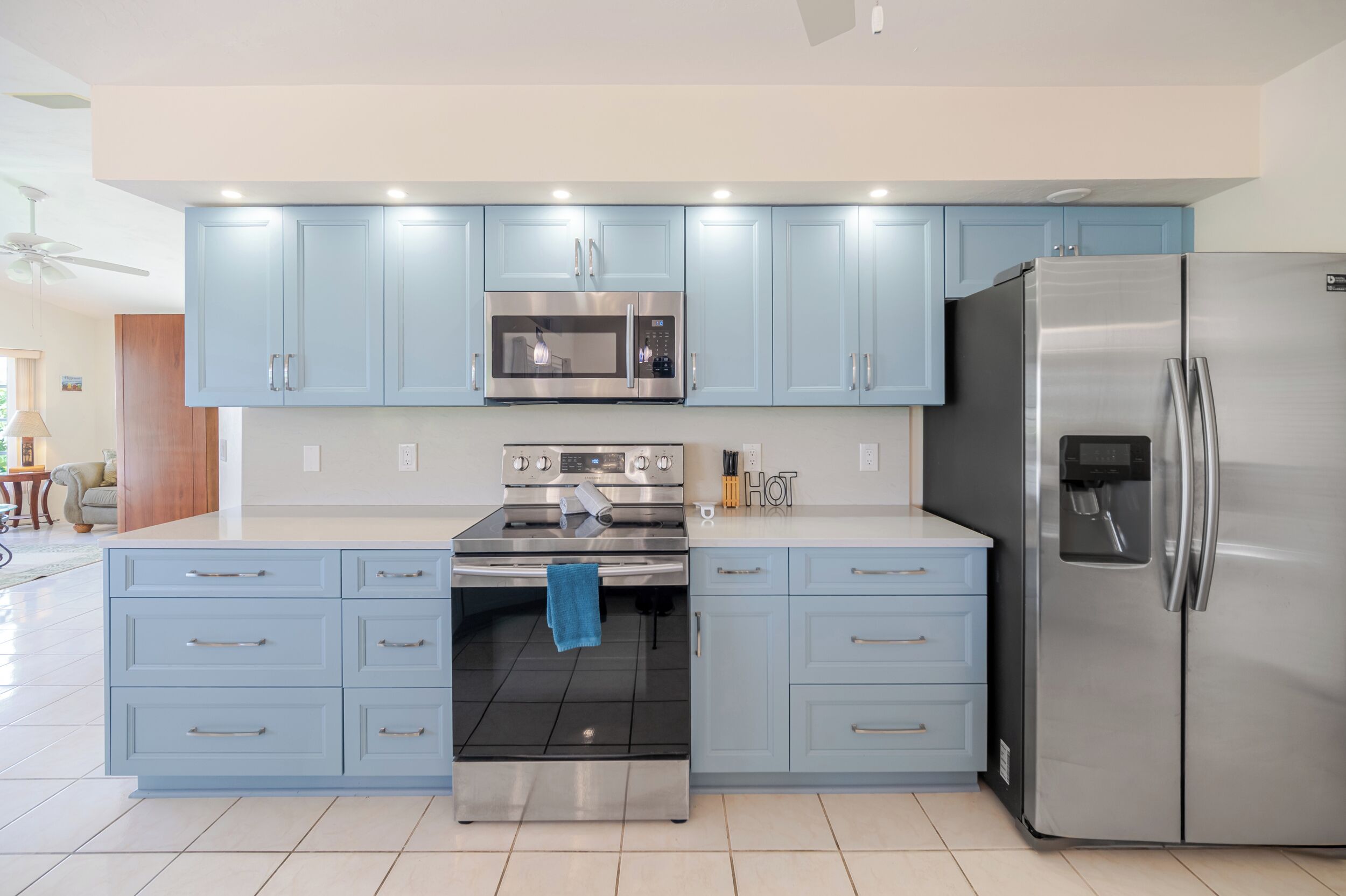 A modern kitchen with light blue cabinets, stainless steel appliances, and a tiled floor.