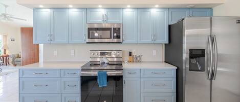 A modern kitchen with light blue cabinets, stainless steel appliances, and a tiled floor.