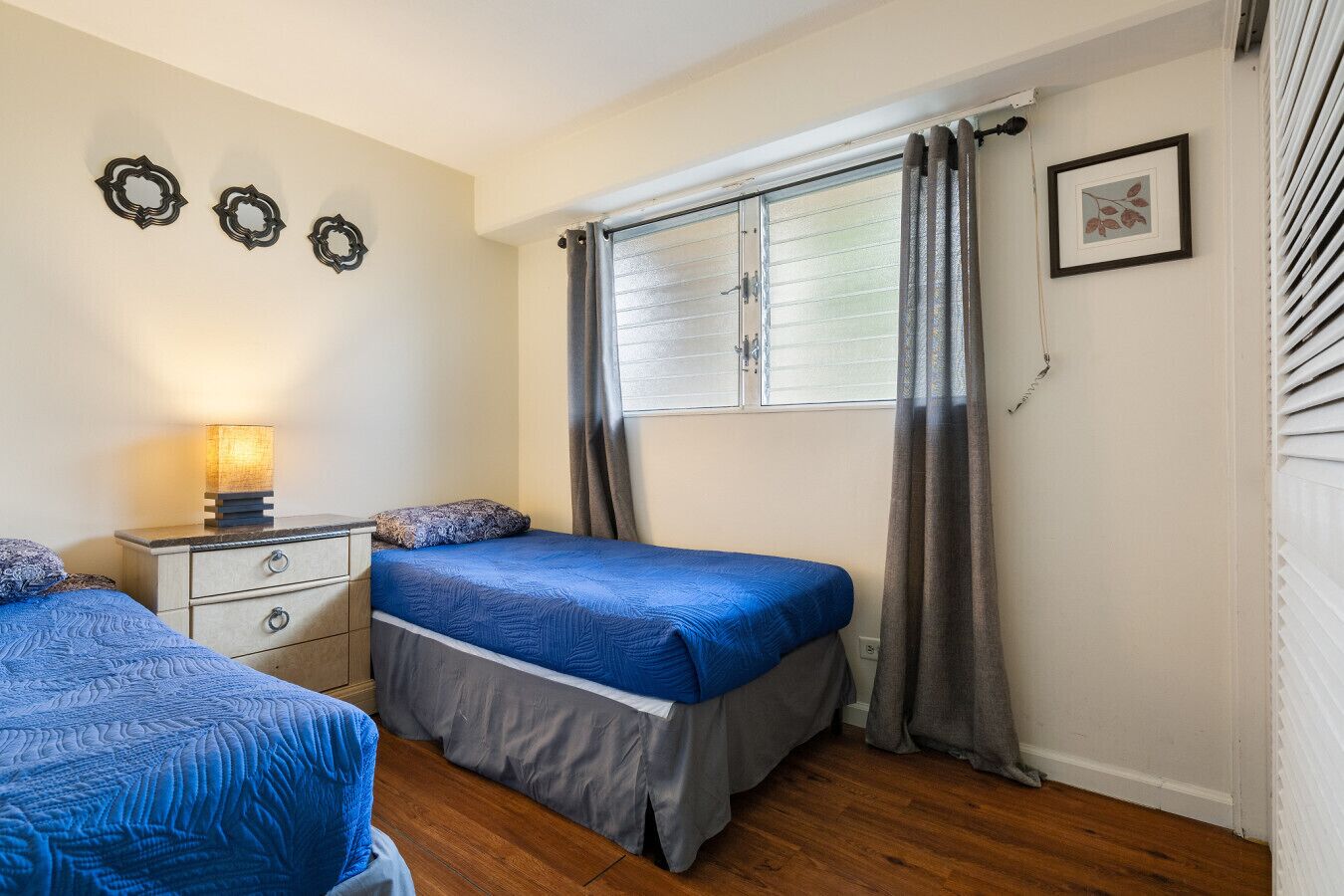 Une chambre avec deux lits, une table de chevet avec une lampe, une fenêtre avec des rideaux et des éléments de décoration murale.