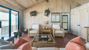 A wooden-floored room with wicker furniture, a ceiling fan, and a view of the sea. - Tree House Atmosphere on Chalk Sound National Park (Providenciales)
