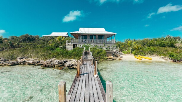 A wooden pier leading to a beachfront property with a white-roofed building and a view of the ocean. - Tree House Atmosphere on Chalk Sound National Park (Providenciales)