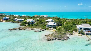 An aerial view of a coastal resort with multiple buildings, clear turquoise waters, and a distant view of the ocean. - Tree House Atmosphere on Chalk Sound National Park (Providenciales)