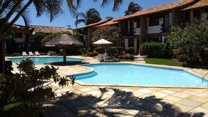 Area piscina con lettini, un ombrellone di paglia e un giardino curato.