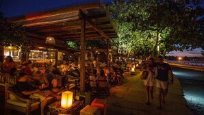 Un ristorante all'aperto con tavoli e sedie in legno, una zona coperta e vista sull'acqua.