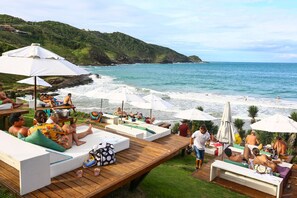 A beachside resort with lounge chairs and umbrellas, a wooden deck, and a view of the ocean and hills.