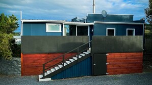 Ein modernes Gebäude mit einer Treppe, die zu einem verschlossenen Eingang führt, umgeben von einer Schotterauffahrt und einer Rasenfläche.