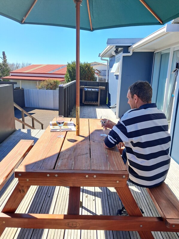 Una terraza de madera con una mesa, sillas, una parrilla y un gran paraguas.