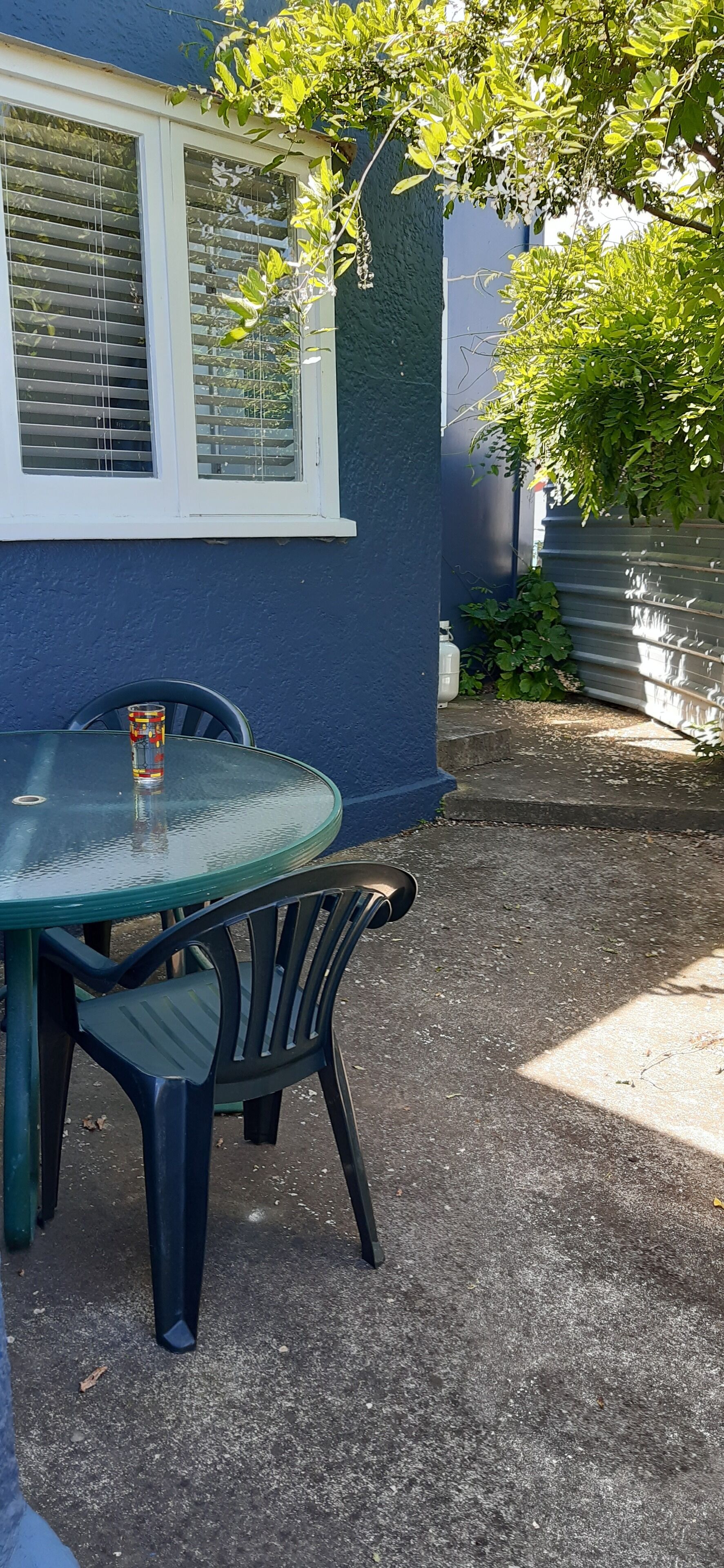 A glass table with a bottle and a chair outside a building with a window.