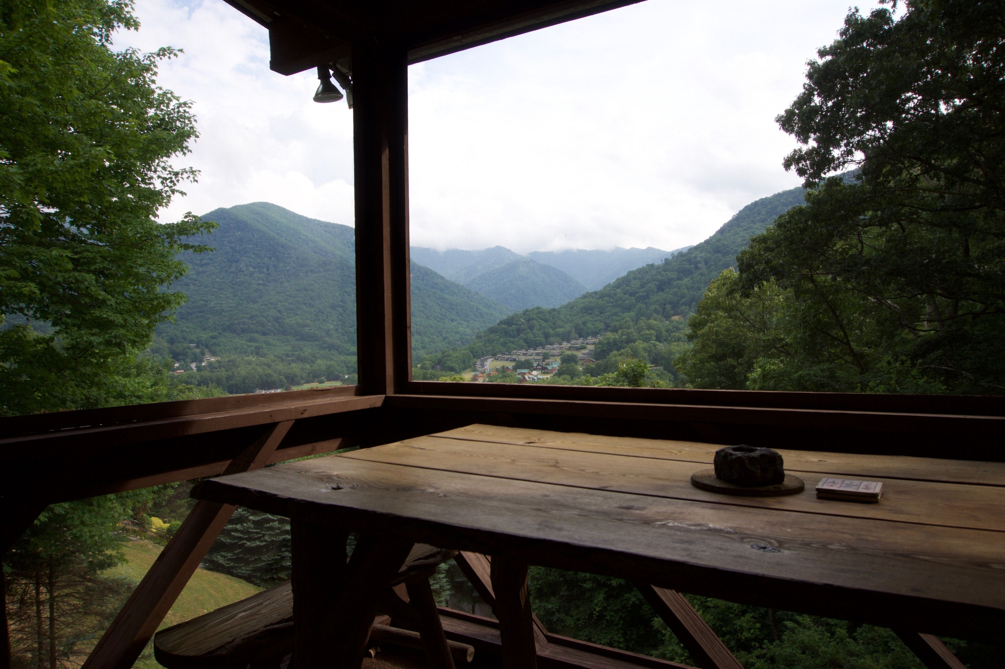 Una mesa de madera con una manta y un libro, con vistas a un valle con montañas y árboles.