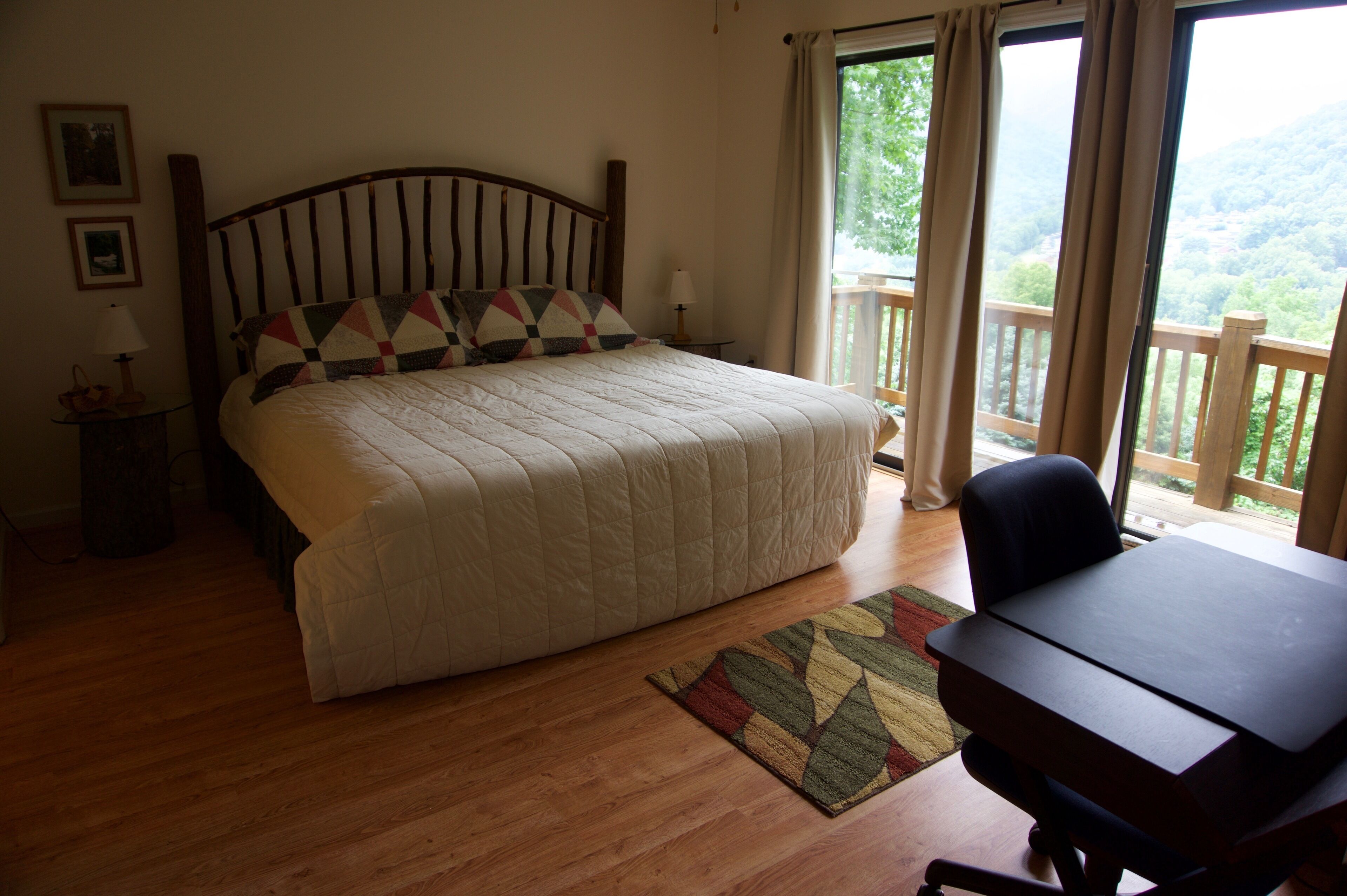 Een slaapkamer met een bed, een bureau, een stoel, een raam met gordijnen en uitzicht op het omliggende landschap.