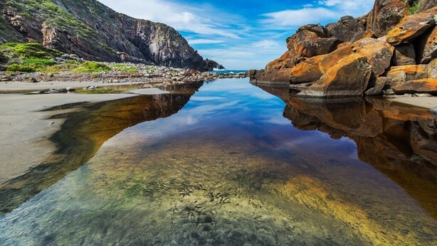 A coastal scene with clear water reflecting the sky and surrounding cliffs. - Deep Creek Homestead (Deep Creek National Park)