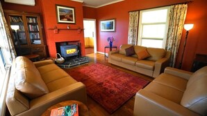 A living room with leather sofas, a fireplace, a bookshelf, and a television. - Deep Creek Homestead (Deep Creek National Park)