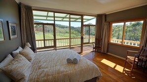 A spacious bedroom with a large bed, a wooden floor, and a balcony with a scenic view. - Deep Creek Homestead (Deep Creek National Park)