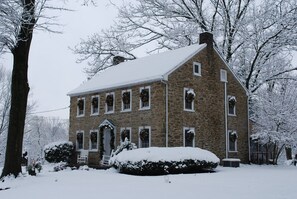 A stone building with multiple windows, a front door, and snow-covered surroundings.
