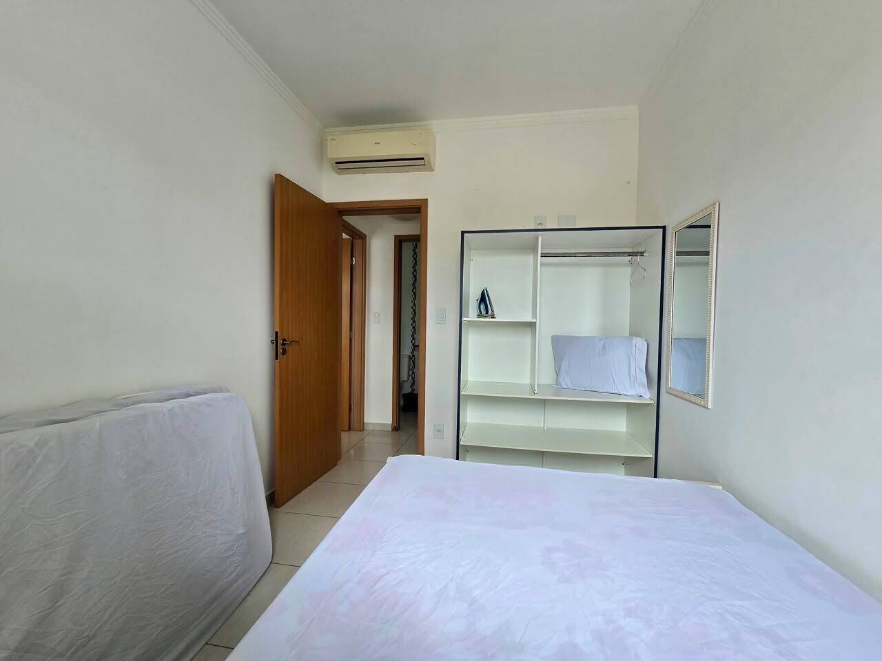 A bedroom with a bed, a wardrobe, a mirror, and an air conditioning unit.