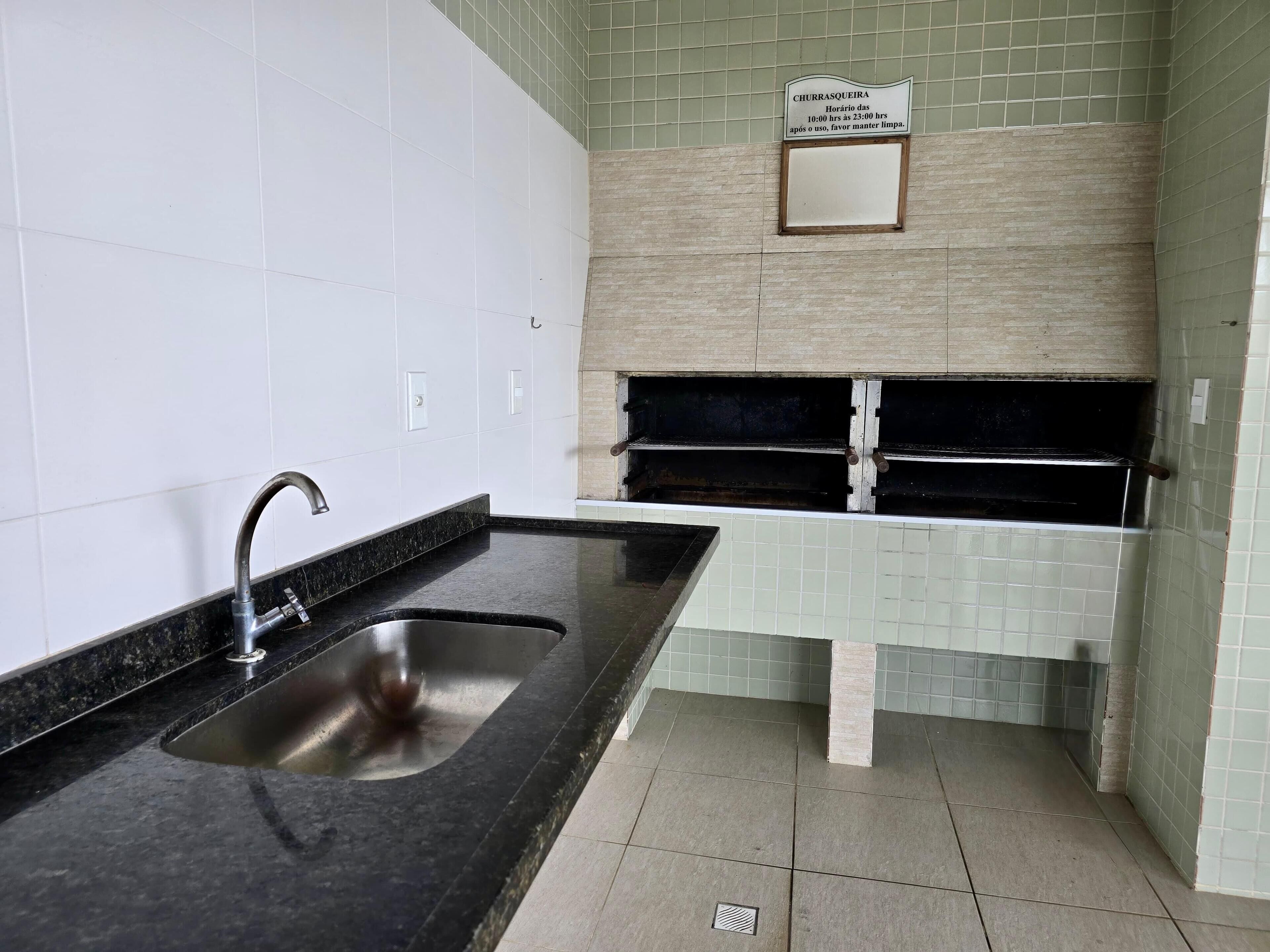 Una cocina moderna con encimera negra, pileta de acero inoxidable y un cartel con el horario de atención.