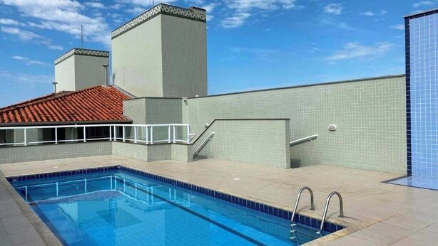 Una piscina con bordo piastrellato, tetto in tegole rosse e un edificio con tetto piatto e camino.