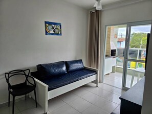 Una habitación con un sofá, una silla, un cuadro y vistas a través de un ventanal.