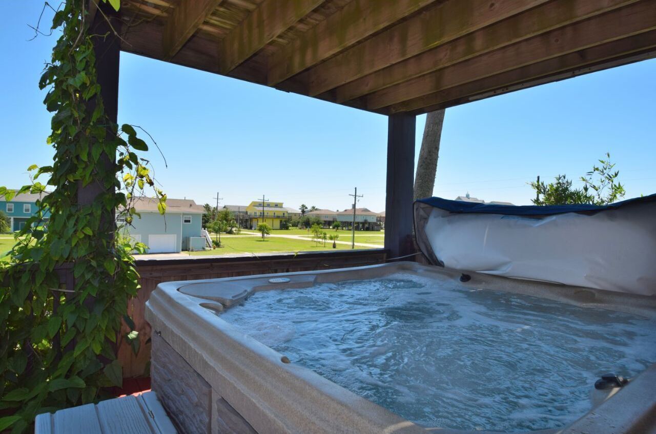 Un jacuzzi bajo una pérgola de madera con vistas a casas y un césped.