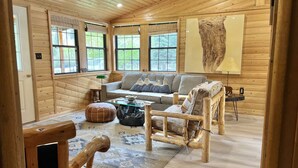 Een knus cabin interieur met houten details, een bank, een stoel, een bijzettafeltje en een vloerkleed.