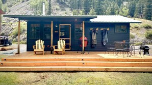Een chalet met veranda, twee Adirondack-stoelen, een barbecue en een tafel met stoelen.