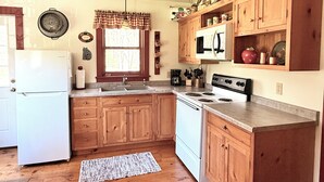 A kitchen with wooden cabinets, a refrigerator, a stove, and a window with curtains. - Cottage on Mink River Road  (Ellison Bay)