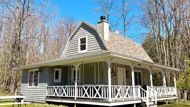 A two-story house with a porch, a chimney, and a satellite dish. - Cottage on Mink River Road  (Ellison Bay)