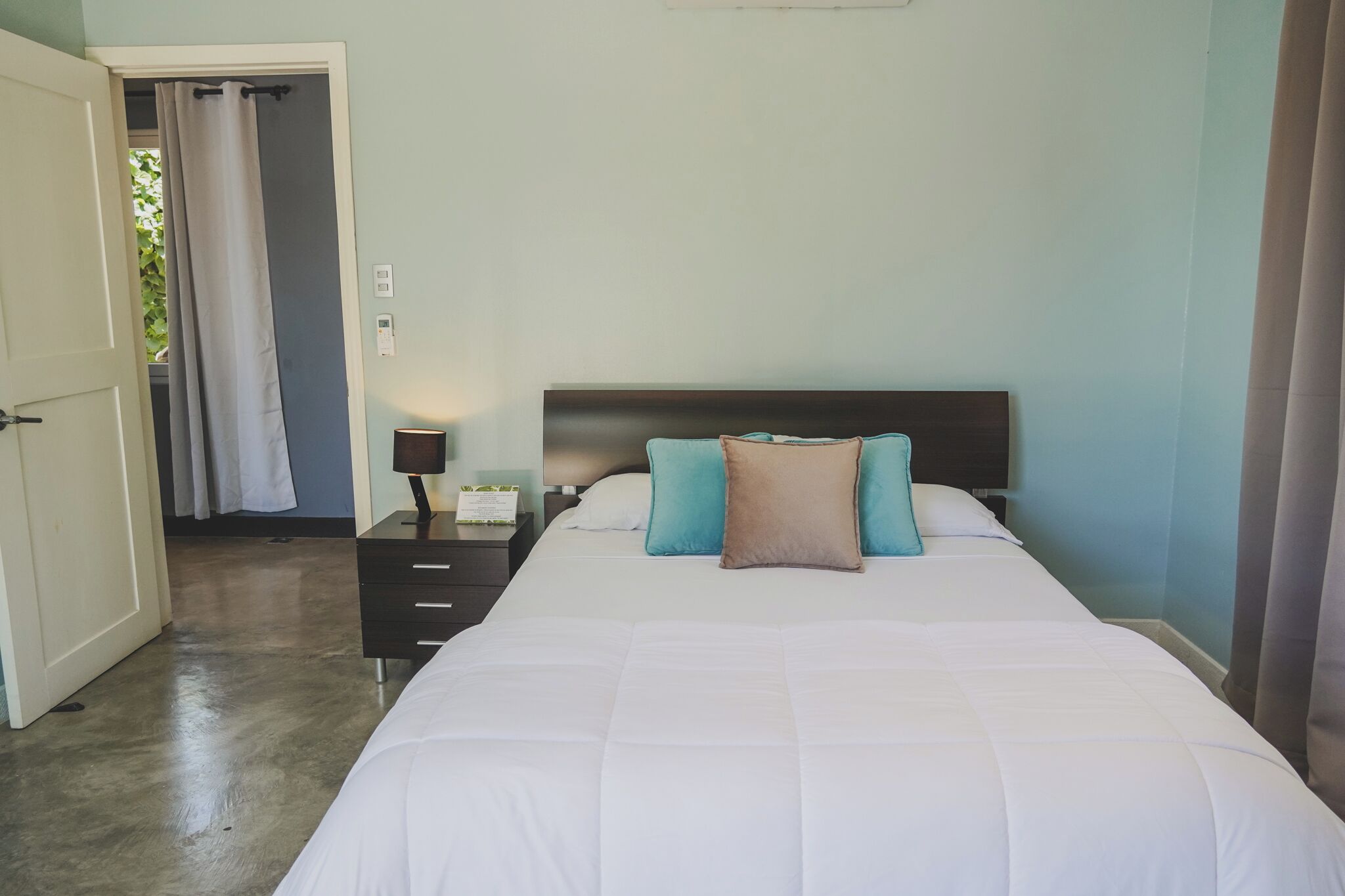 Quarto com cama, mesa de cabeceira, luminária e porta para o banheiro.