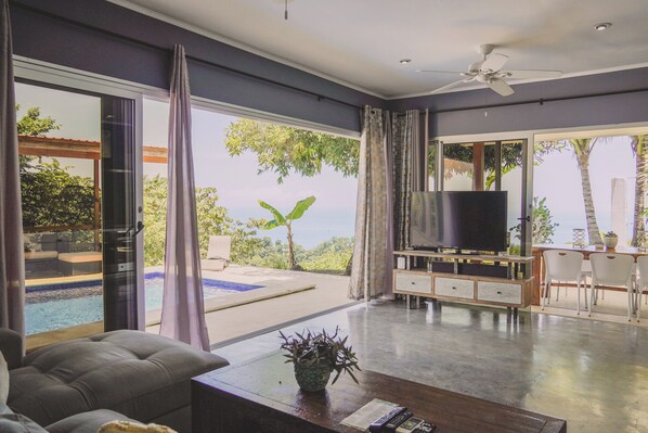 Un salón moderno con televisor de pantalla plana, sofá, mesa de centro y vistas a una piscina y zonas verdes.