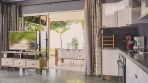A modern kitchen with white cabinets, a built-in oven, and a coffee maker. There is a dining area with a table and chairs, and a TV on a wooden stand. - Casa La Colina Oceanview Villa Santa Teresa Beach (Santa Teresa Beach)