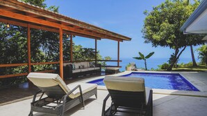 A poolside area with lounge chairs, a wooden pergola, and a view of the ocean. - Casa La Colina Oceanview Villa Santa Teresa Beach (Santa Teresa Beach)