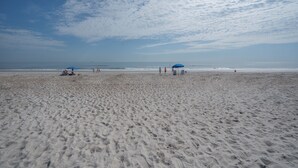 Una spiaggia sabbiosa con impronte, due ombrelloni blu e cielo sereno.