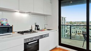 A modern kitchen with white cabinetry, a stove, a microwave, and a dishwasher. There's a large window offering a city view.
