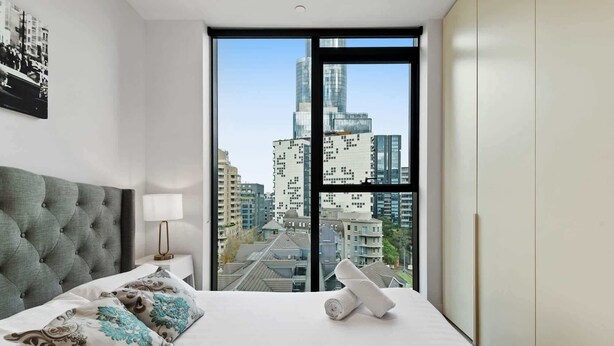 A modern hotel room with a large bed, a view of a cityscape, and a city skyline through floor-to-ceiling windows.