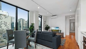 A modern living room with a city view, a dining area with chairs and a table, and a kitchen with a stove.