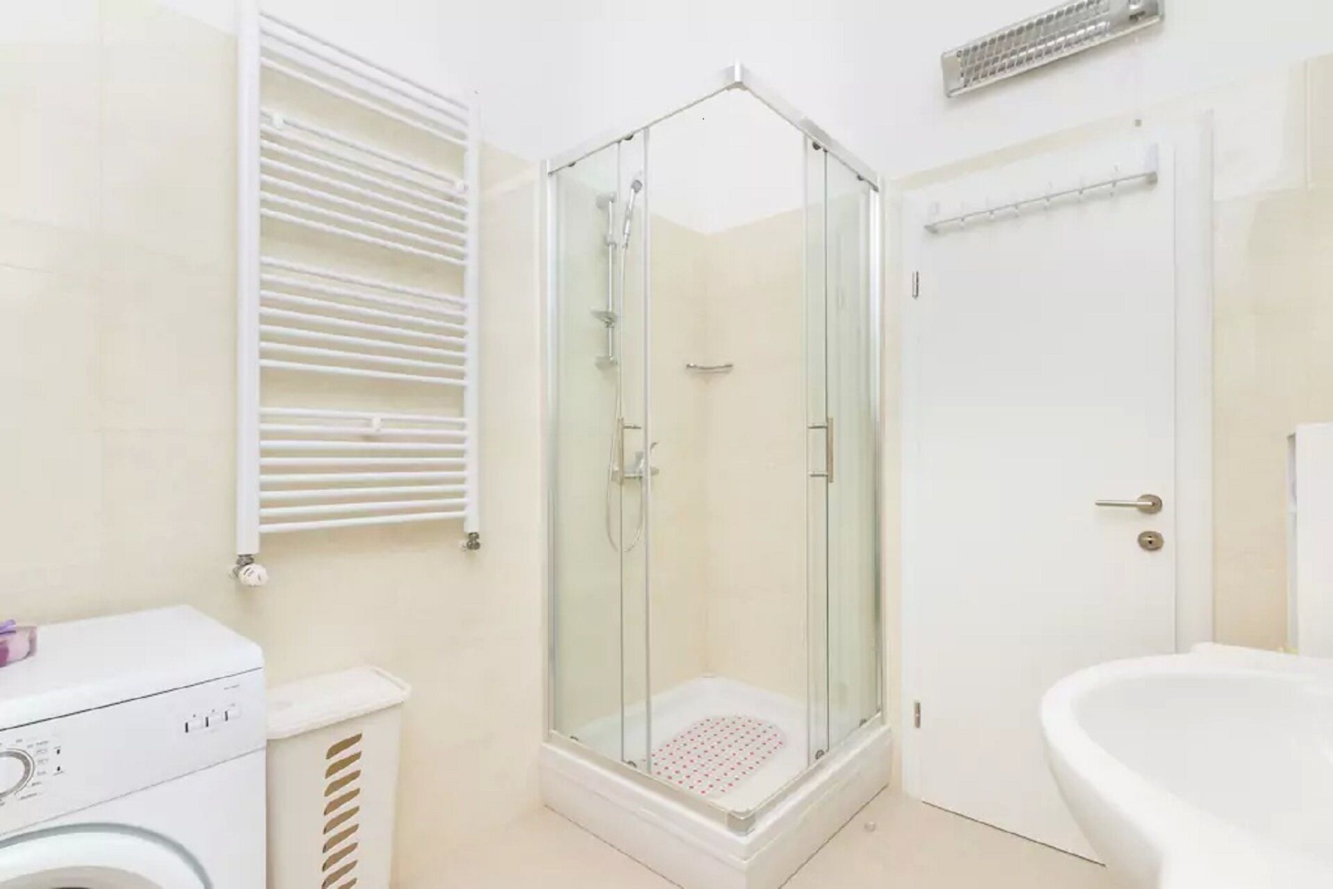 Un baño moderno con ducha envuelta en vidrio, lavabo blanco y lavadora.