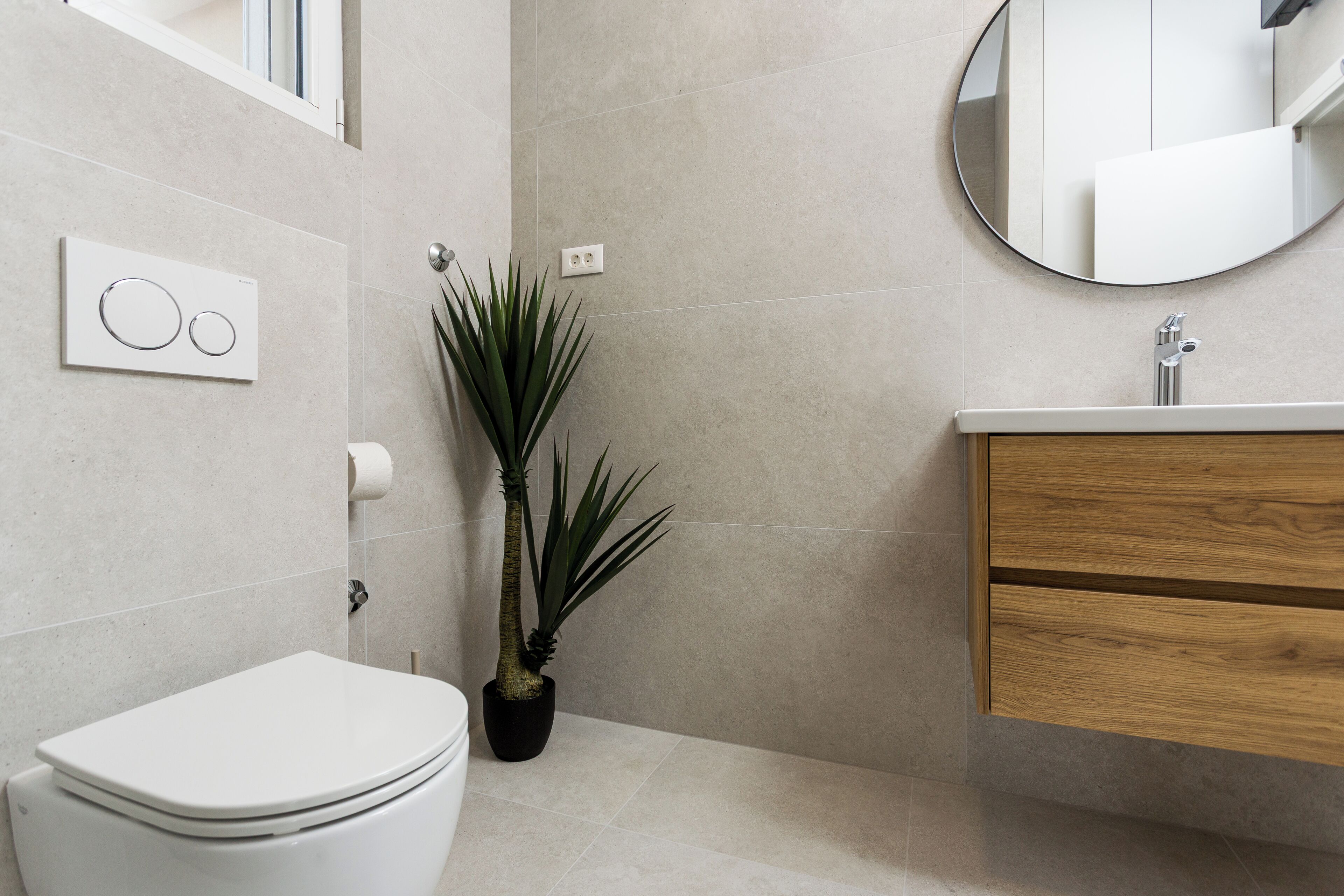 Bagno con WC, lavandino, specchio, una pianta in vaso e interruttore della luce a parete.