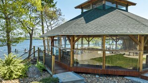 Un belvédère en bois doté d’une structure vitrée, offrant une vue sur un lac, et entouré de sentiers pavés et de verdure.