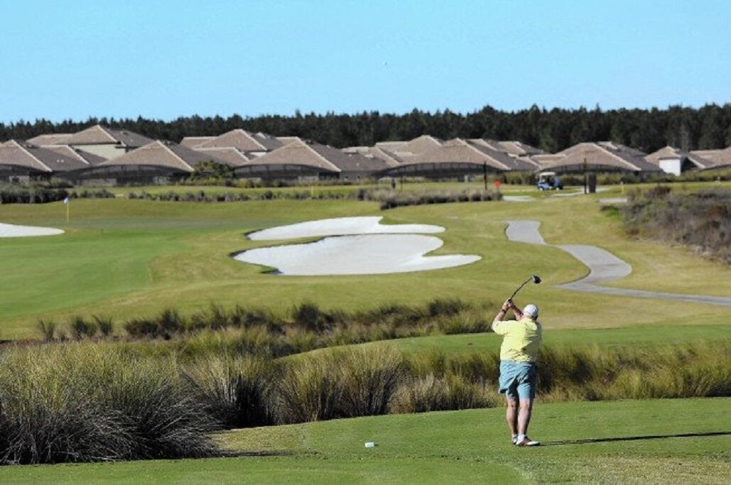 Ein Golfplatz mit Bunkern, einem Putting-Green und einem Clubhaus im Hintergrund.