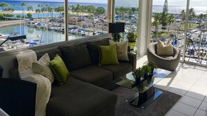 A modern living room with a large window overlooking a marina and beach. - New Decor! Oceanfront, Yacht Harbor, Luxury, Friday Fireworks front row, FAB! (Honolulu)