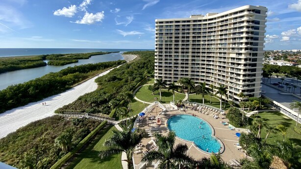 A high-rise hotel with a pool, surrounded by greenery and a beach. - Newly Renovated Beach Condo with 2 Kings...Awesome Pool, Beach and Sunset Views (Marco Island)