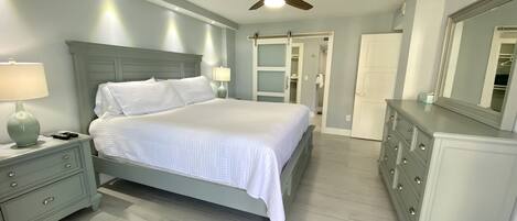 Un dormitorio con cama, mesitas de noche, cómoda, ventilador de techo y vestidor.